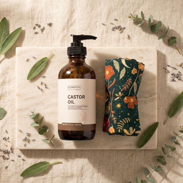 Bottle of castor oil with a floral castor oil pack on a textured surface with leaves.